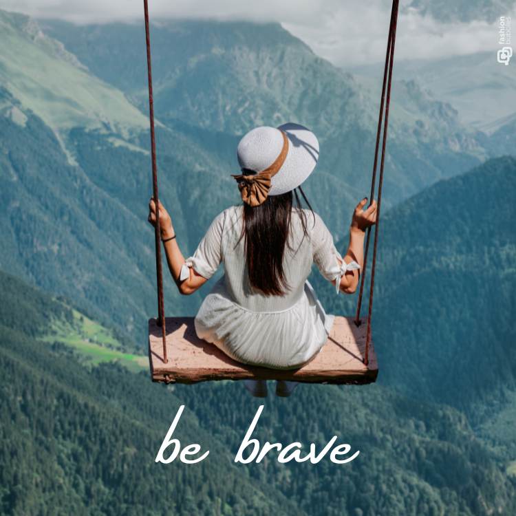 Escrito "Be brave" em foto de mulher balançando em balanço alto com fundo de montanhas.