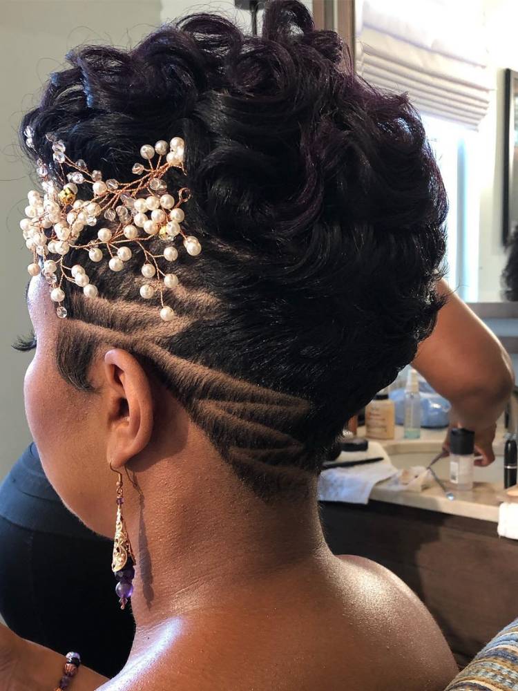 Noiva de pele negra de costas, com cabelo curto raspado na lateral, acessório de pérolas e cachos no topo