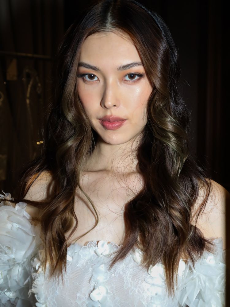 Mulher asiática com vestido de noiva, cabelo ondulado solto e maquiagem natural