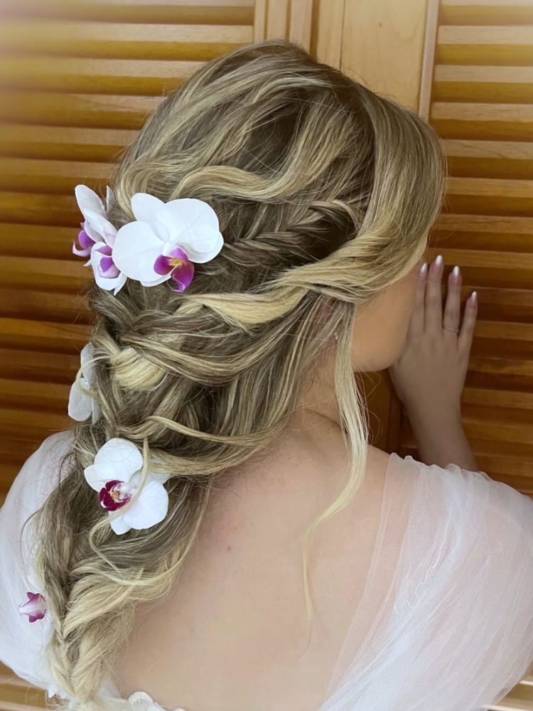 Mulher de pele clara vestida de noiva de costas usando trança no cabelo com flores brancas e rosas