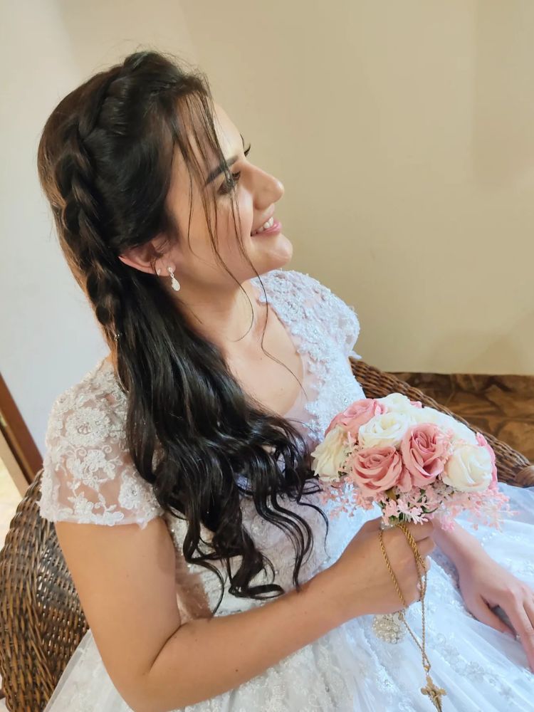 Mulher de pele clara usando vestido de noiva, segurando um buquê de flores rosas e com cabelo solto com trança