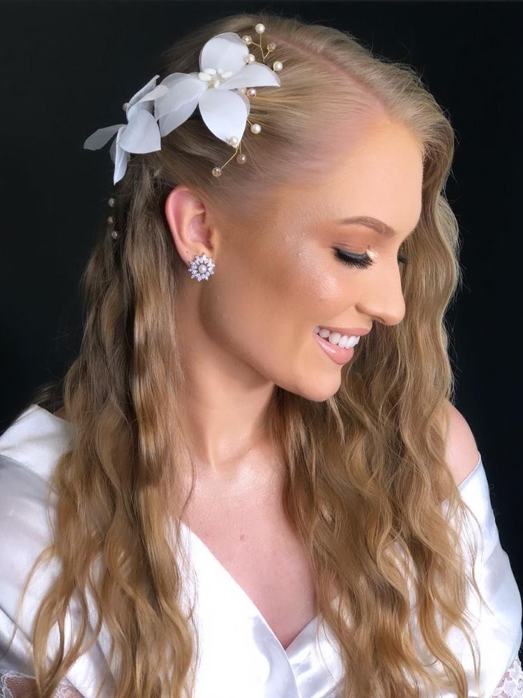 Mulher de pele clara vestida de noiva, usando maquiagem clean e cabelo triondas com flor branca