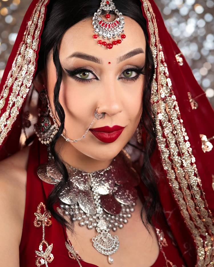 Influenciadora Camila Pudim com roupa indiana vermelha e prata e make olhos delineados e batom vermelho
