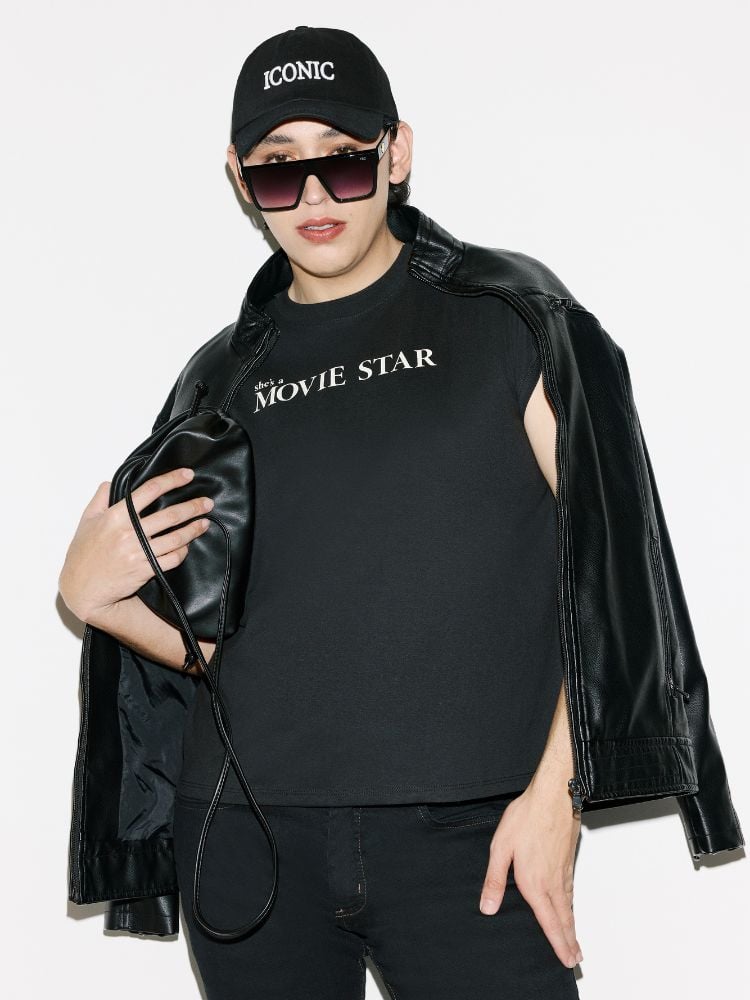 Gabb usando óculos de sol, boné preto, jaqueta preta, bolsa preta e camiseta preta escrito "she's a movie star"