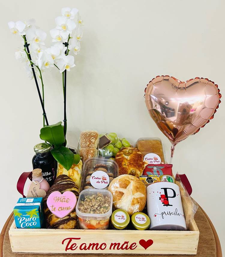 cesta com orquídea, balão, pães, sucos, doces, canecas e frutas