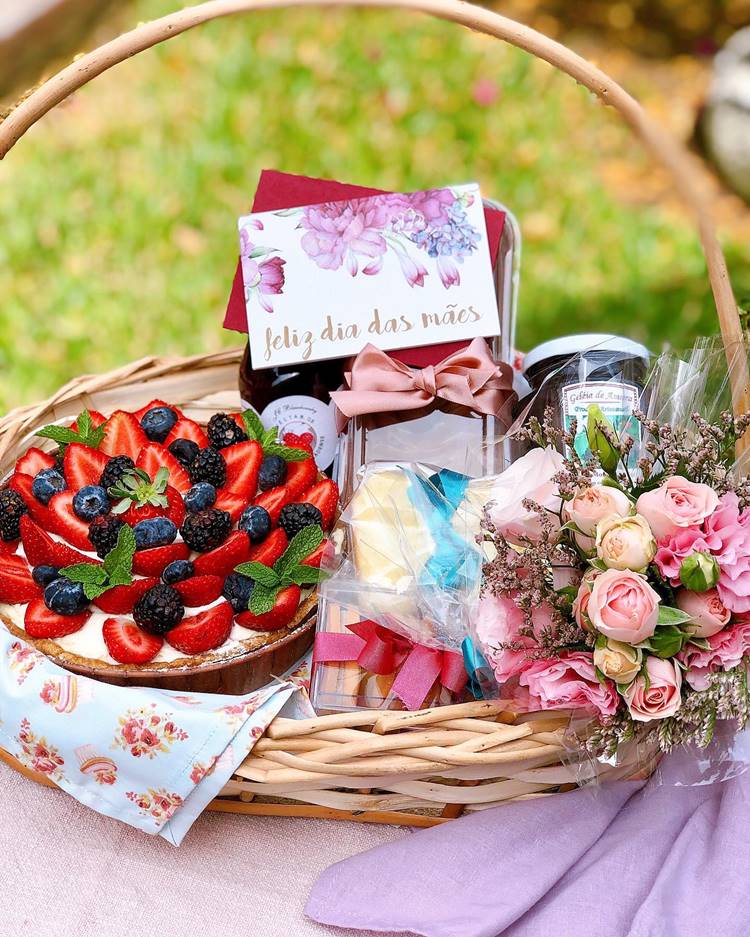 cesta com bolo de frutas vermelhas, geleia de amora, macarrons e buquê de flores