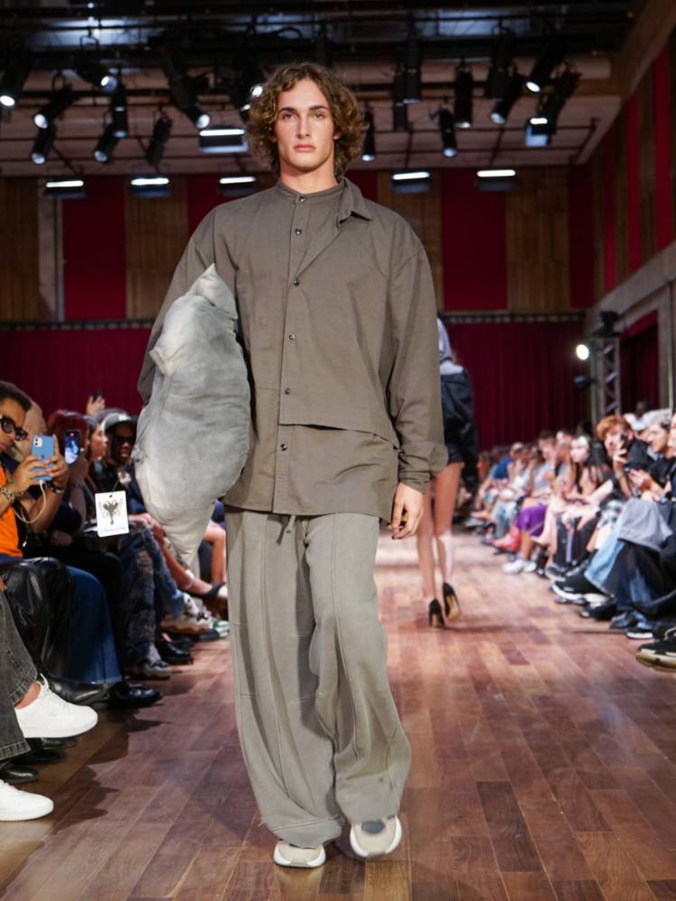 Homem de pele clara usando blusa de manga longa marrom e calça cinza