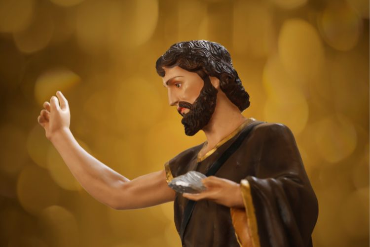 Foto de pequena escultura de São João em fundo dourado