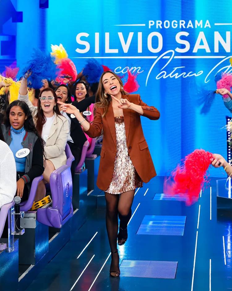 Patrícia Abravanel com look de paetês, meia calça preta e blazer marrom apresentando o programa Silvio Santos, na plateia