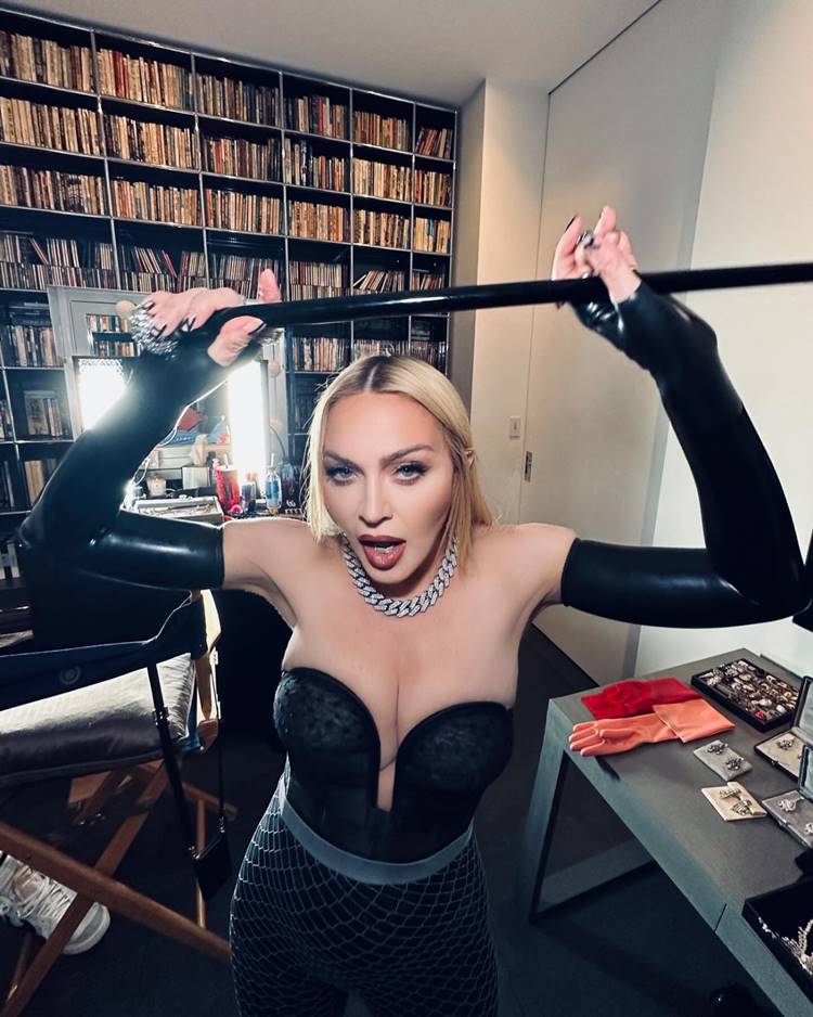 Cantora Madonna com roupa preta de corset decotado segurando uma muleta preta
