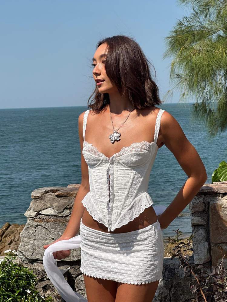 Mulher asiática em praia usando corset com alças finas e minissaia, ambos em branco