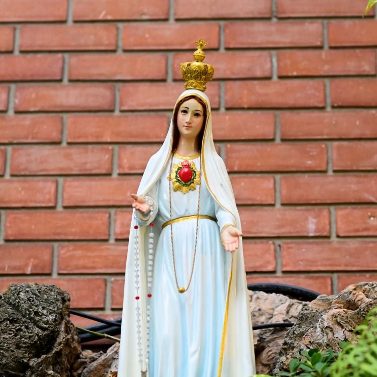 Foto de imagem de Nossa Senhora de Fátima em volto de pedras em fundo de parede de tijolinhos