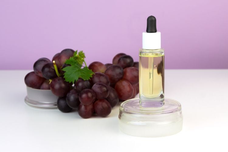 Foto de uvas ao lado de frasco com conta-gotas. Ao fundo, uma parede roxa