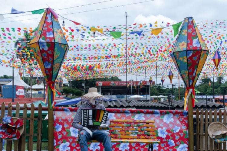 Festa de São João ao ar livre, com balões coloridos, bandeirinhas e boneco tocando saxofone