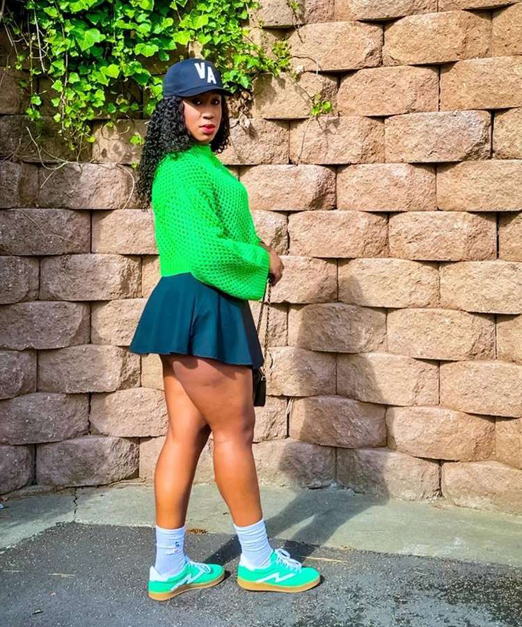 Mulher com look usando short-saia curta + cropped de crochê verde neon + boné + tênis verde com meia