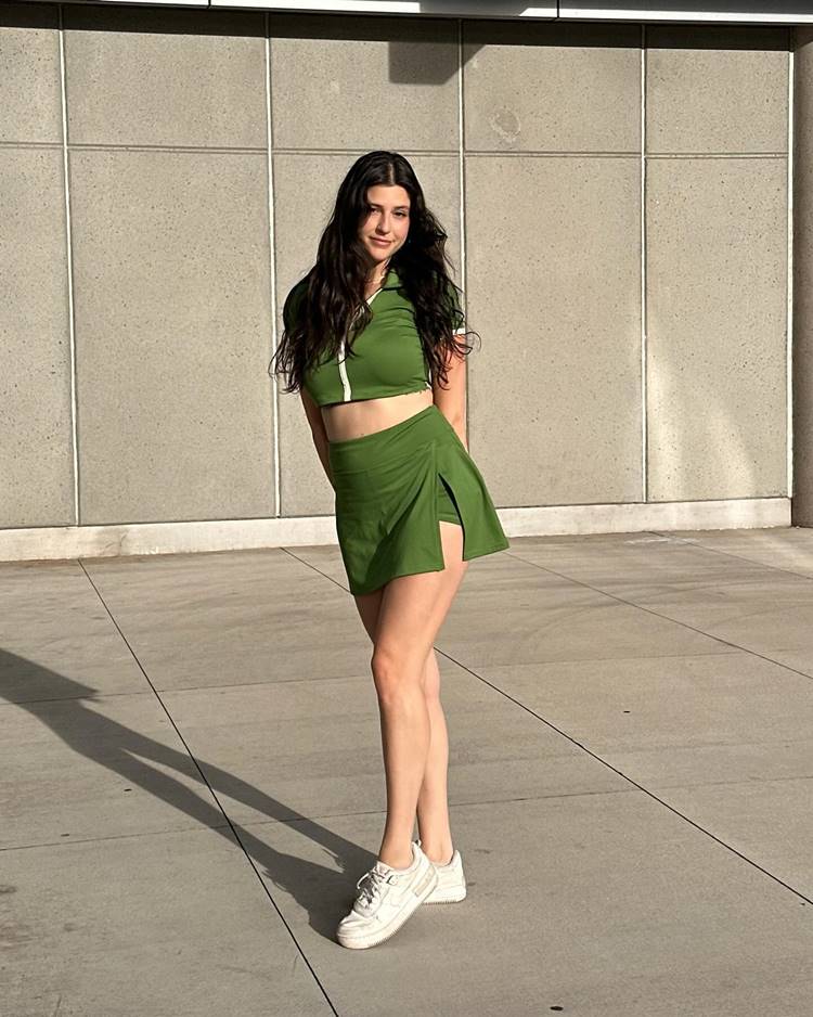 Mulher com look usando short-saia e cropped esportivo verde militar + tênis branco 