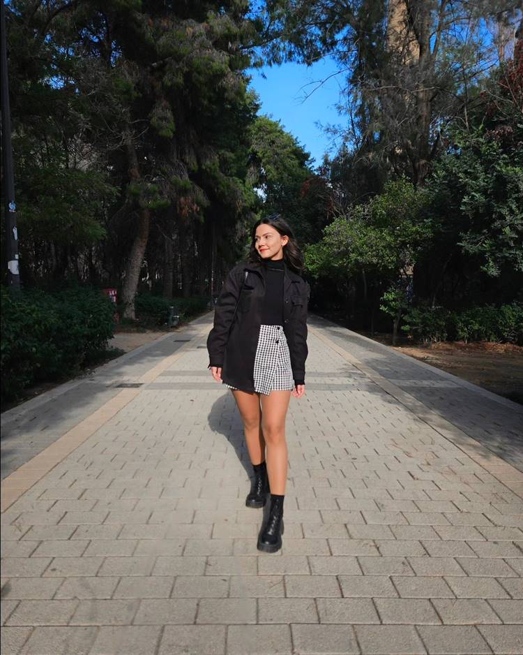 Mulher com look usando skort xadrez + blusa preta + jaqueta preta + coturno preto