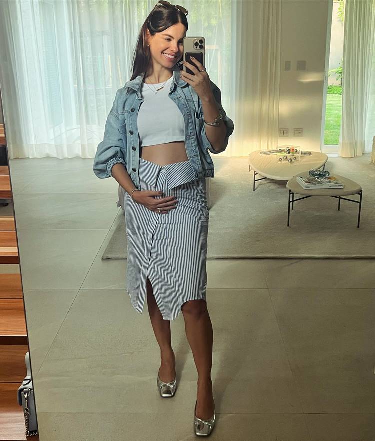 Atriz Sthefany Brito grávida em 2024 usando cropped branco, saia de listra mid e jaqueta jeans em foto no espelho