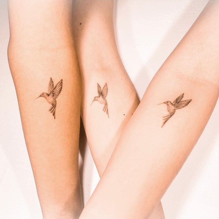 Três braços com tatuagem de beija-flor