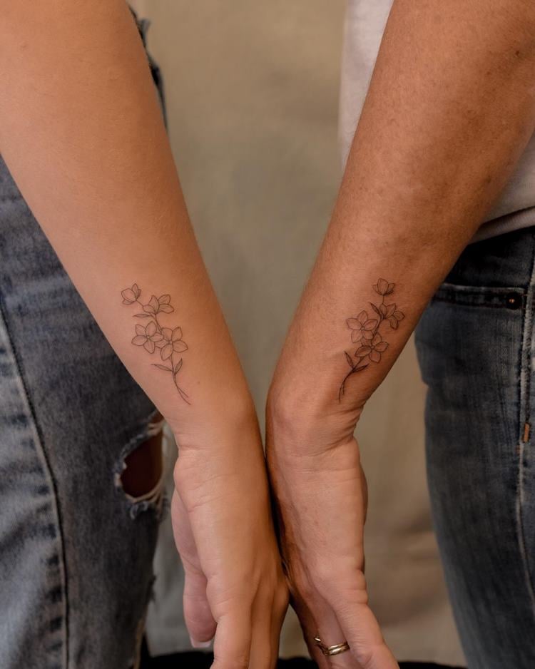 Tatuagem delicada de ramo de flor em braço, próximo do pulso, em dois braços