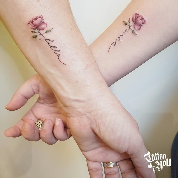Tatuagens delicadas de flor com nome mãe em uma e filha em outro em braços, próximo do pulso