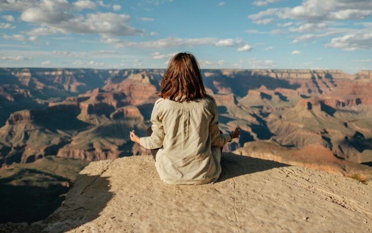 Mulher morena de costas com as mãos em meditação, olhando para paisagem de montanha para desenvolver a espiritualidade