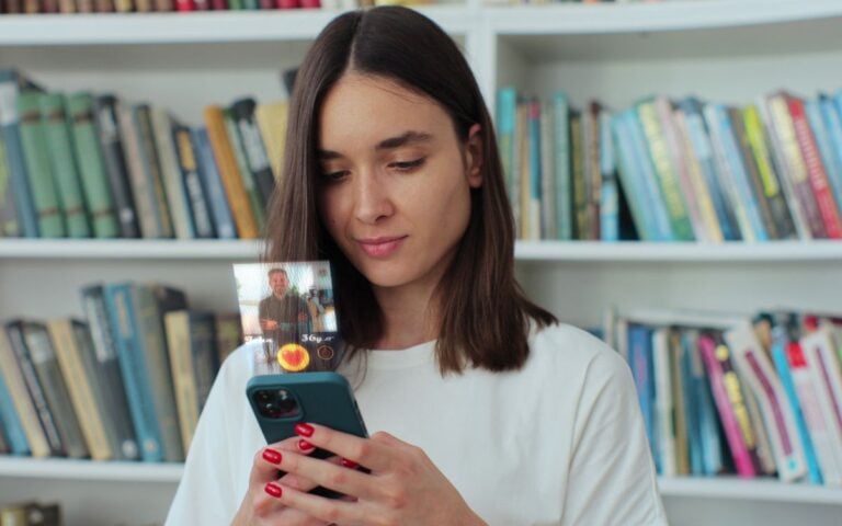 Mulher de cabelos castanhos médios, usando camiseta branca e usando o celular para comunicação virtual em aplicativo de relacionamento