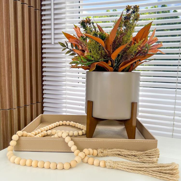 Mesa branca com bandeja de couro bege, vaso cinza com planta e cordão bege