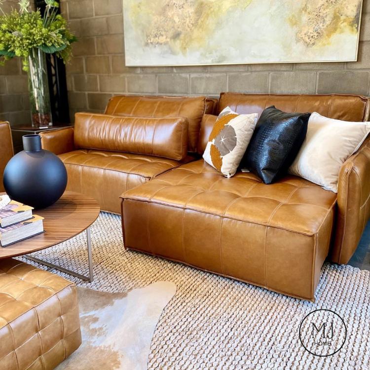 Sala com sofá marrom de couro, tapete bege, almofadas coloridas, vaso azul, planta, quadro e mais itens decorativos 