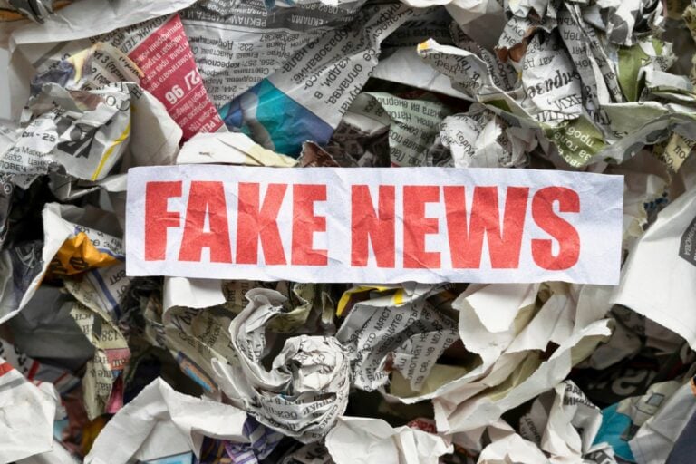 Papel escrito Fake News com jornais amassados no fundo
