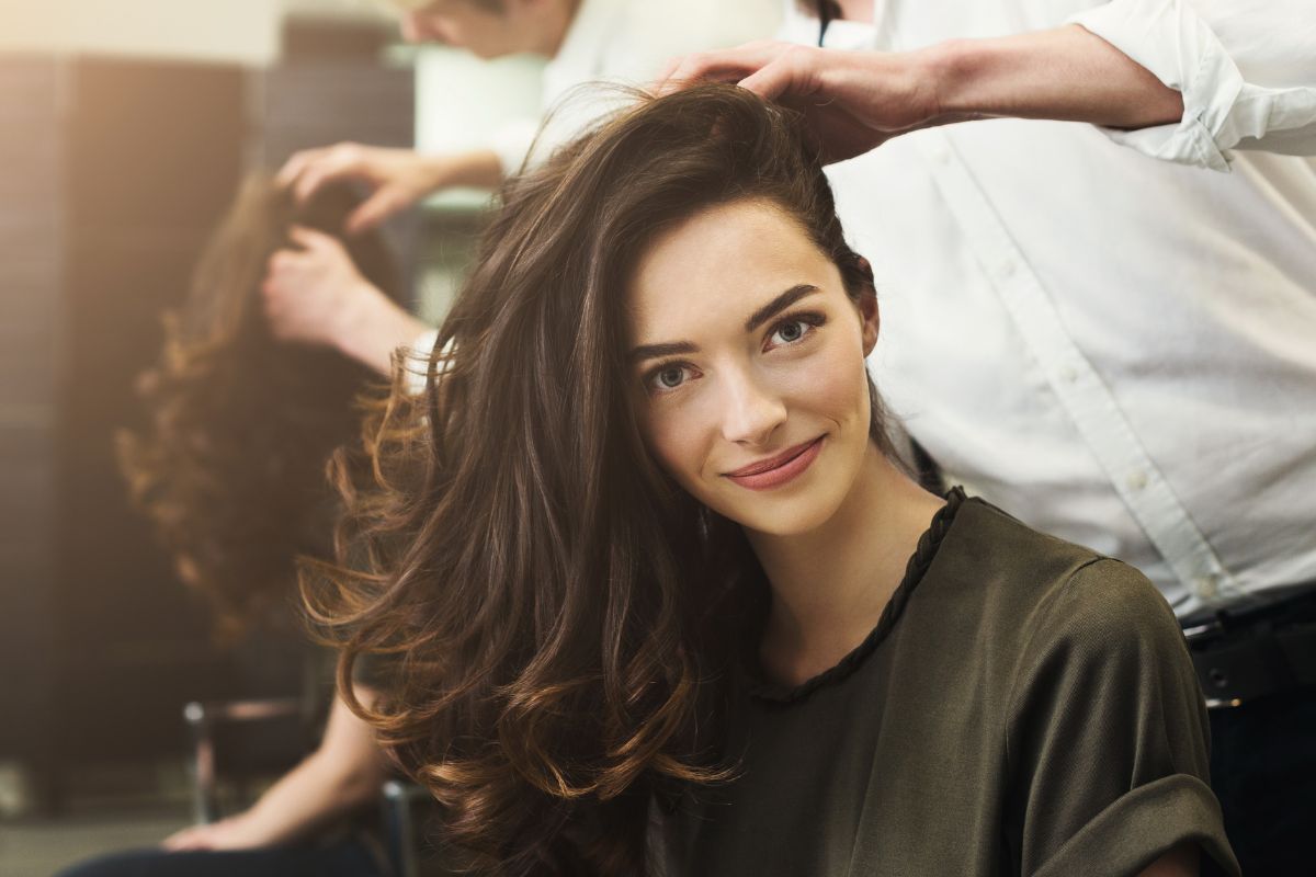 Foto de mulher de cabelo castanho com cabeleireiro mexendo no cabelo dela