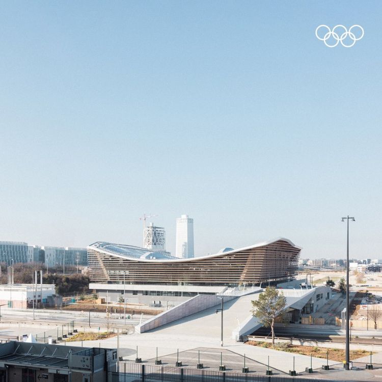 Centro Aquático das Olimpíadas de Paris ao longe, com céu limpo e símbolo das Olimpíadas em branco no canto superior direito