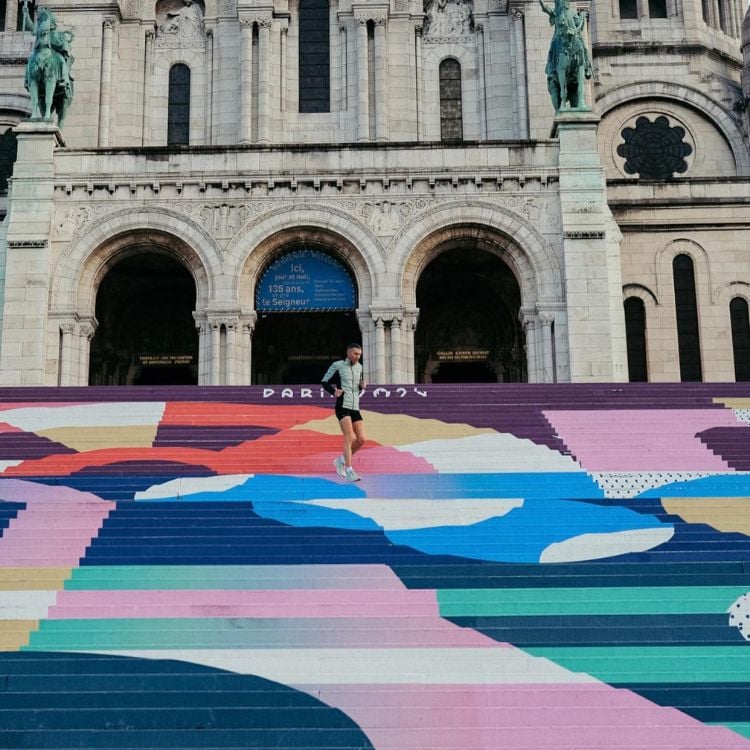 Pessoa de pele clara descendo escada da Sacré Coeur, colorida e escrito "Paris 2024"