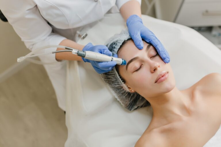 Mulher de pele clara deitada em maca, usando touca e recebendo tratamento estético facial