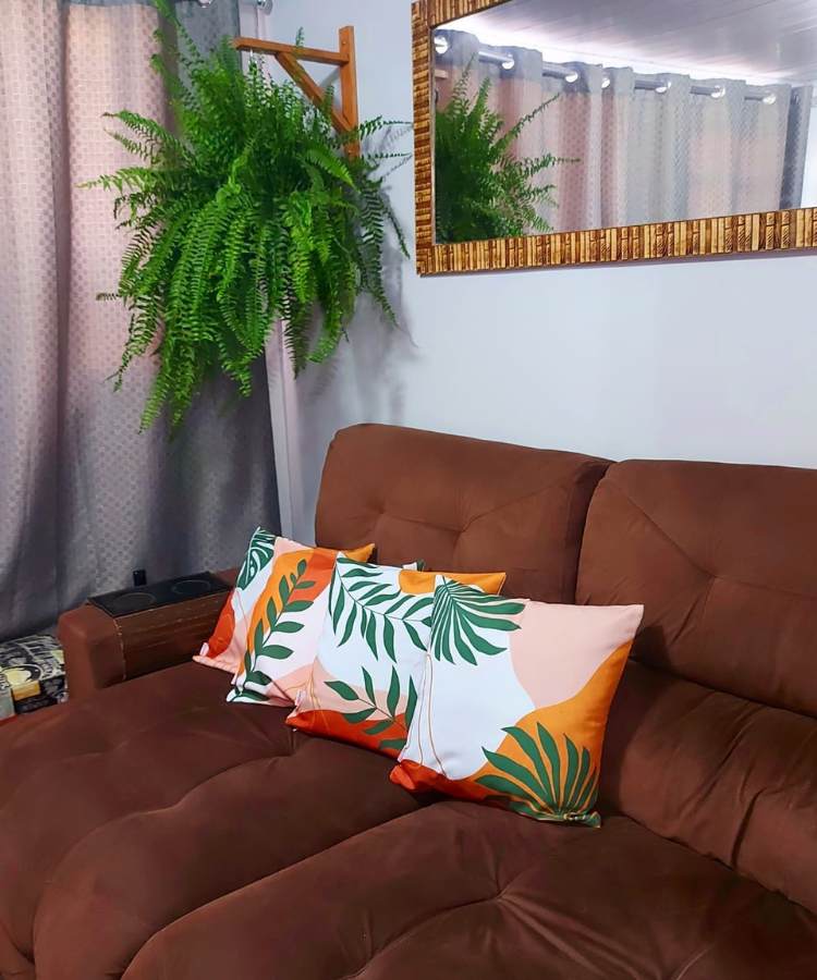Sala com sofá marrom, almofadas, espelho e planta samambaia no canto