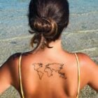Foto de mulher com tatuagem de mapa-múndi nas costas. Ela está de biquini na praia