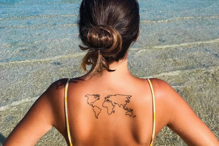 Foto de mulher com tatuagem de mapa-múndi nas costas. Ela está de biquini na praia
