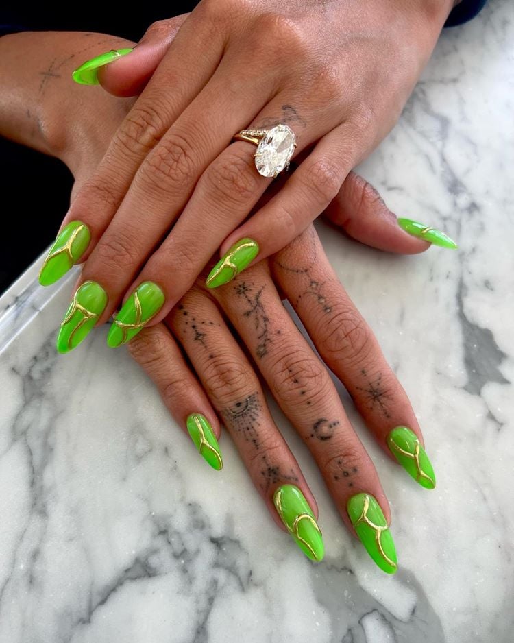 Mãos de Hailey Bieber com unhas decoradas verde limão comt extura dourada