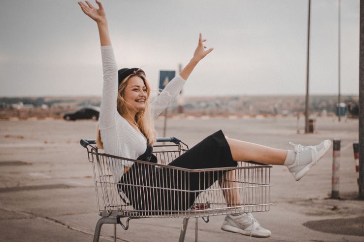 Mulher loira usando blusa branca e calça preta dentro de um carrinho de supermercado