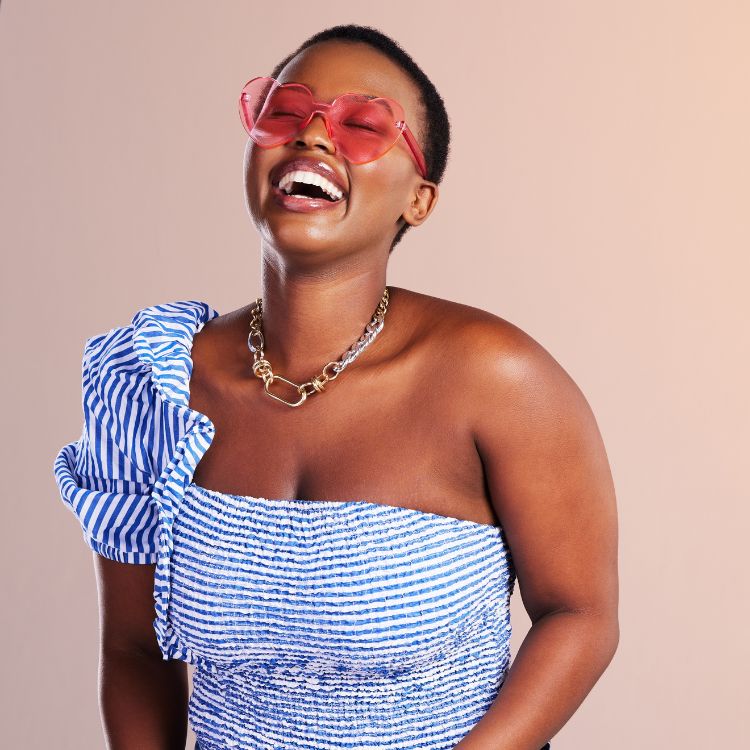 Garota negra sorrindo com óculos formato de coração, colar e vestido azul listrado