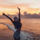 Jovem mulher na praia fazendo sinal de paz e amor com as mãos para cima
