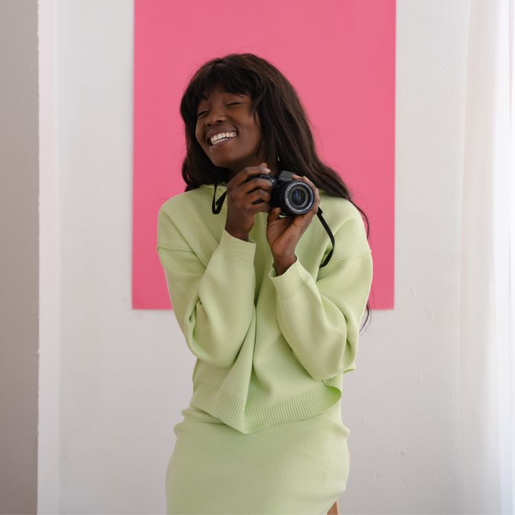 Menina negra usando look verde menta e segurando câmera fotográfica