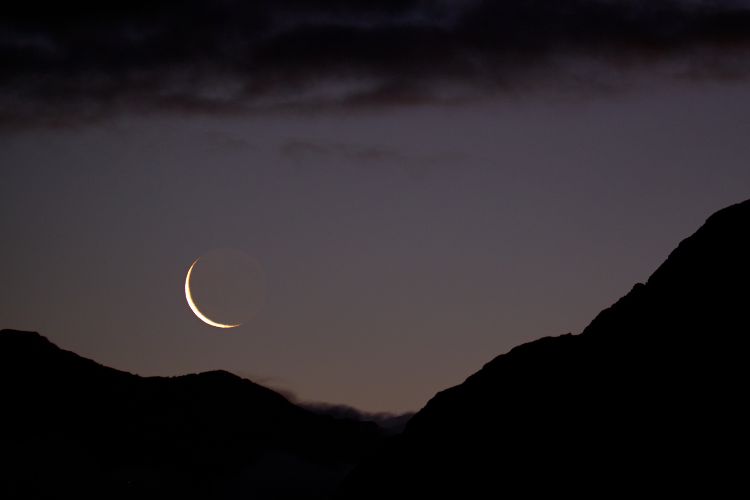 Foto de montanhas à noite. No céu, vemos a Lua Nova