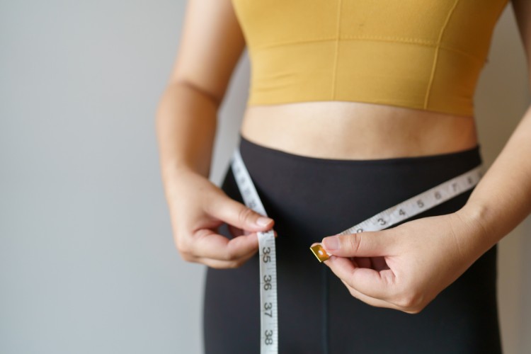 Mulher de pele clara usando cropped amarelo e legging preta, passando fita métrica na cintura