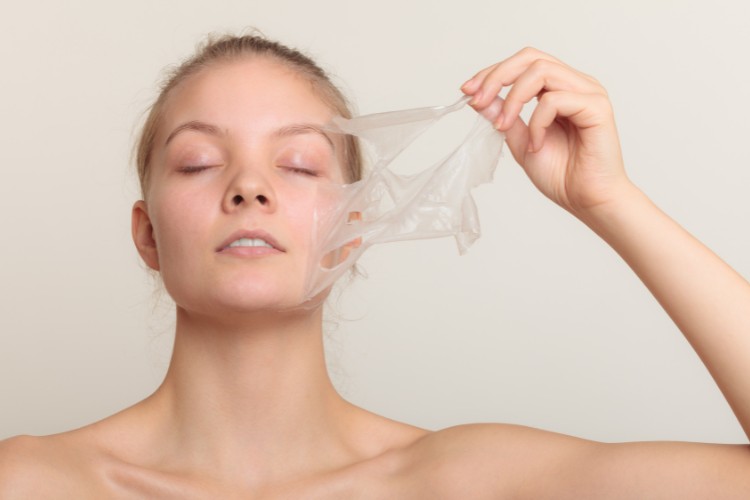 Mulher loira de pele clara tirando máscara facial transparente