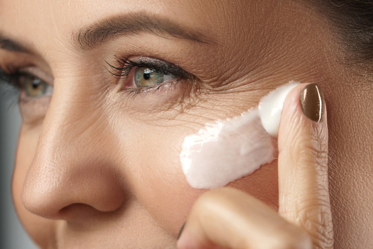 Mulher de pele clara e olho verde com algumas rugas nos olhos aplicando protetor solar