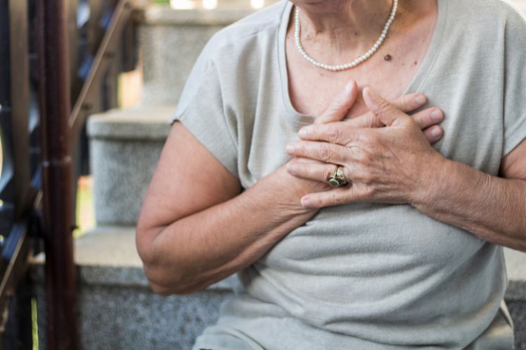 Mulher idosa com falta de ar, com as mãos no peito, sentada em escada