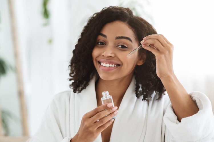 Mulher negra com roupão aplicando sérum com retinol no rosto