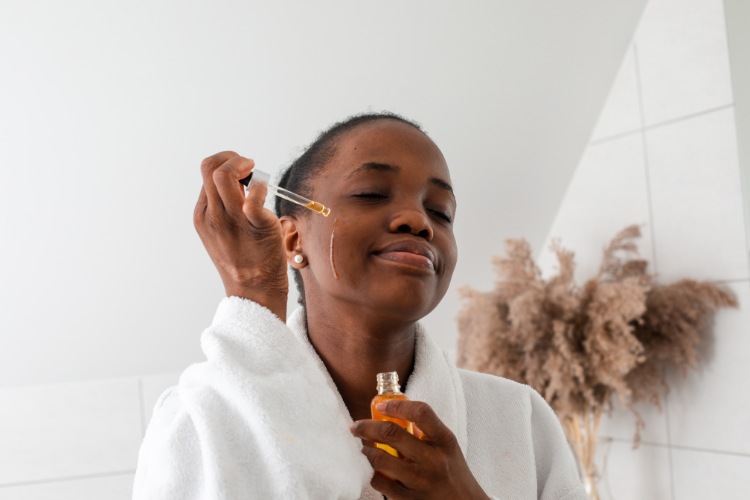 mulher com roupão aplicando vitamina c sérum no rosto no banheiro