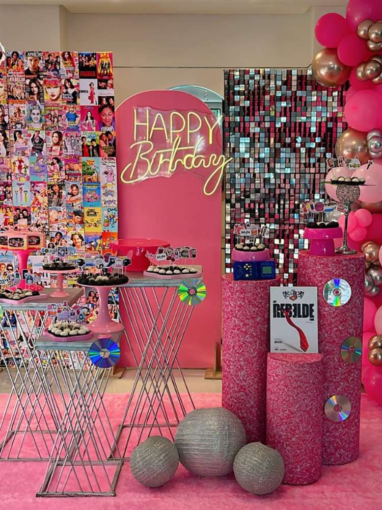 Foto de festa anos 2000 em rosa, com capas de revista, disco ball, cds e muito mais